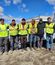 Six field workers in safety vests and work gear lined up against company vehicles, displaying teamwork in industrial setting