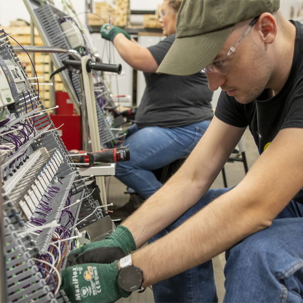 A man wearing safety glasses and gloves focuses on wiring a terminal block assembly.