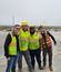 Four field team members in hard hats and safety vests posing together on construction site, with power lines visible in background