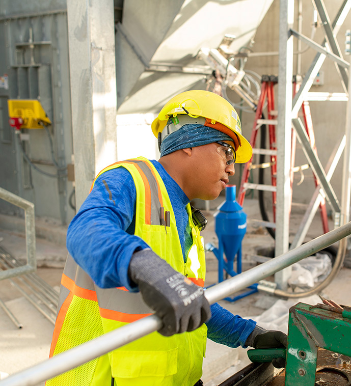 An employee in PPE gear like a hard hat and vest holds conduit.
