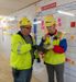 Two employees in hard hats look at a tablet.