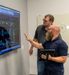 Two Employees Analyzing Data on TV Screen