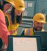 three people in PPE in a manufacturing setting looking at screens and smiling