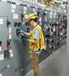 Technician in safety gear inspecting electrical switchgear panels in an industrial facility