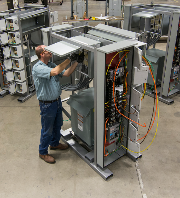 A technician at Interstates wires a large electrical control panel, with visible cable management and internal components in a well-lit shop.