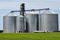 View of 4 grain bins in a grain elevator in an open area with green grass.