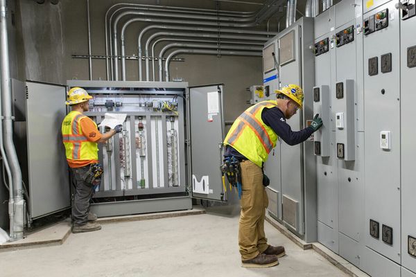 Two men in PPE working in an electric room.