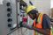 Field technician in hard hat and high-visibility vest performing detailed electrical panel installation or maintenance work