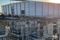 Early morning view of an industrial construction site with organized electrical conduit installations and steel framing in progress. A large metal building structure stands in the background under the rising sun, showcasing precision electrical infrastructure work and modern industrial development.