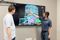 Two men standing in front of a wall-mounted screen reviewing a colorful 3D model of a structural framework.