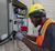 Electrician in safety gear working inside an open electrical control panel.