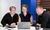 Four coworkers smile while reviewing a tablet and laptop together at a desk in an office.