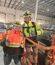 Two workers in hard hats and high-visibility gear giving thumbs up while working on industrial equipment in warehouse setting