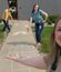 Colleagues showcase sidewalk art featuring a chalk hopscotch course and rainbow, taking selfie-style photo while gesturing to their creations