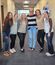 Six casual-dressed office workers standing together in a workplace hallway, wearing complementary neutral-toned outfits
