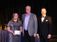 three people standing on a stage accepting an award