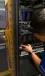 A technician in a server rack points to a small touchscreen on a rack-mounted system inside a data center cabinet.