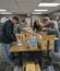Several employees standing around a table packing items into cardboard boxes in a workspace setting.