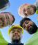 Low-angle selfie of four workers forming a circle looking down at camera, one wearing Interstate hard hat, with bright blue sky background
